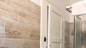 A bathroom with wooden wall tiles, a white door, and a glass shower enclosure. - Dani's House - affittacamere (Cagliari)