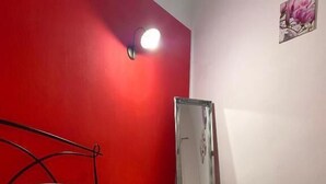 A hotel room with a red accent wall, a bed with white linens, a bedside table, and a mirror. - Dani's House - affittacamere (Cagliari)