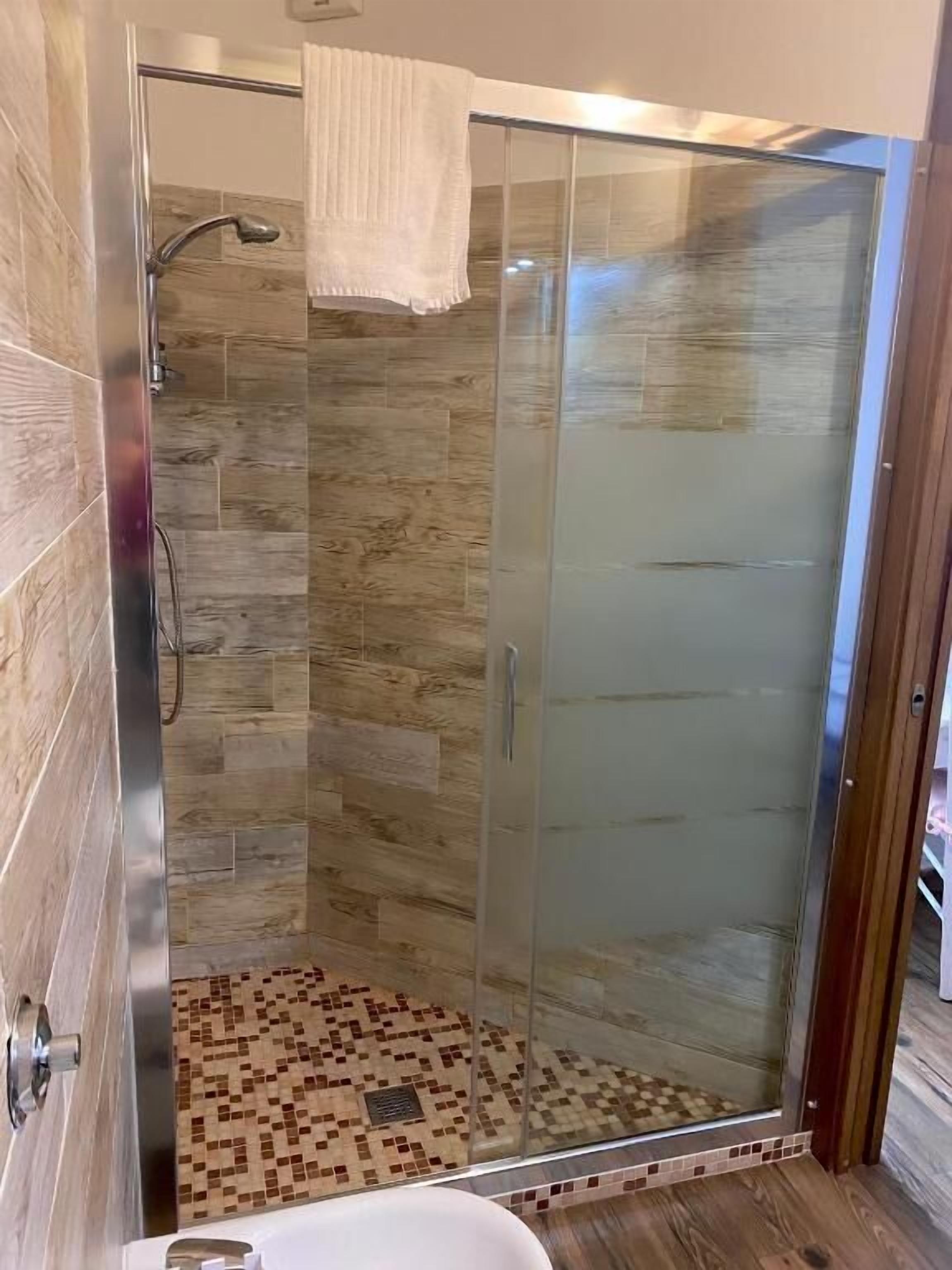Una ducha con paredes de vidrio, suelo de baldosas y una toalla blanca colgada en la puerta.