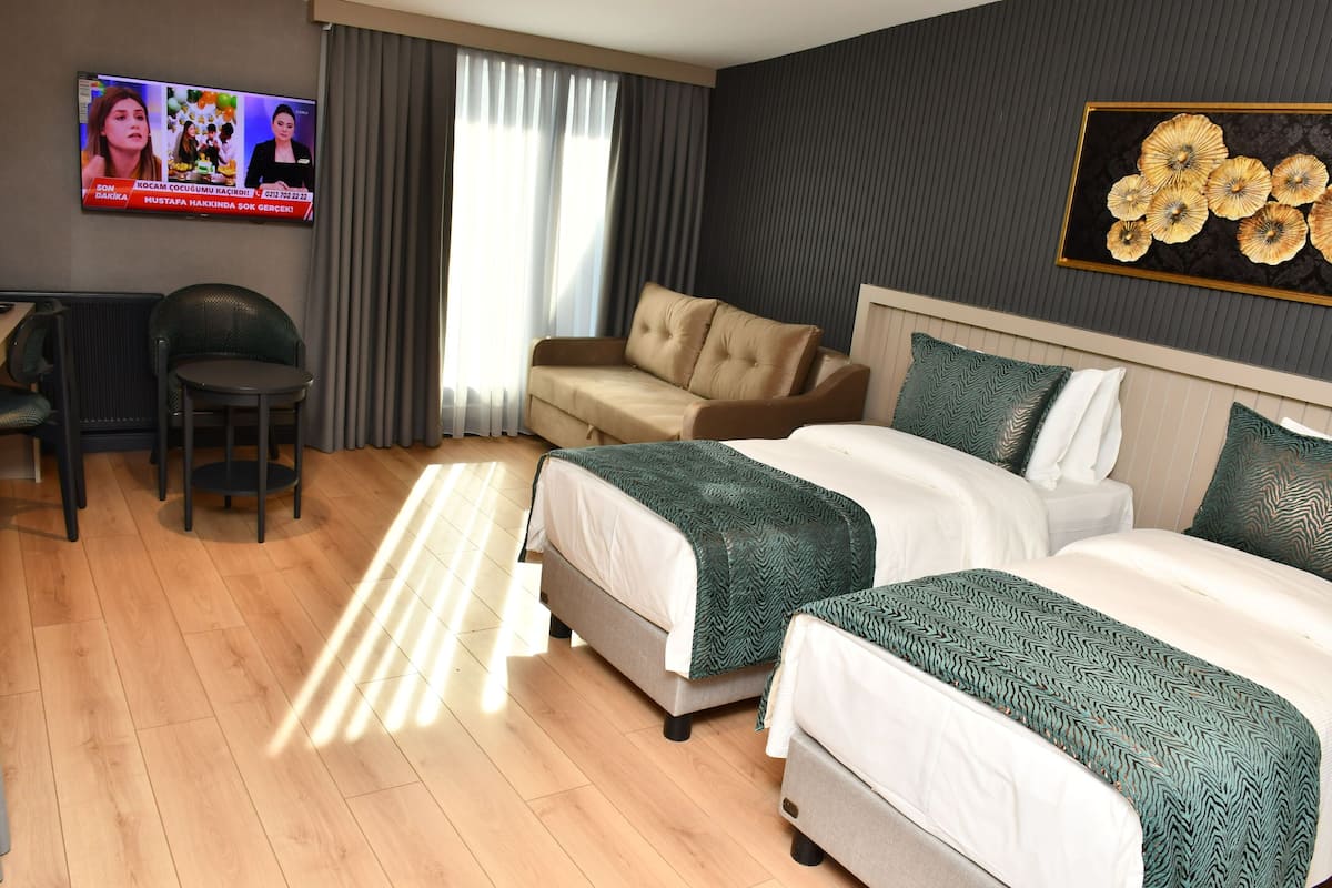 Quarto de hotel com duas camas, um sofá, uma televisão e uma secretária.