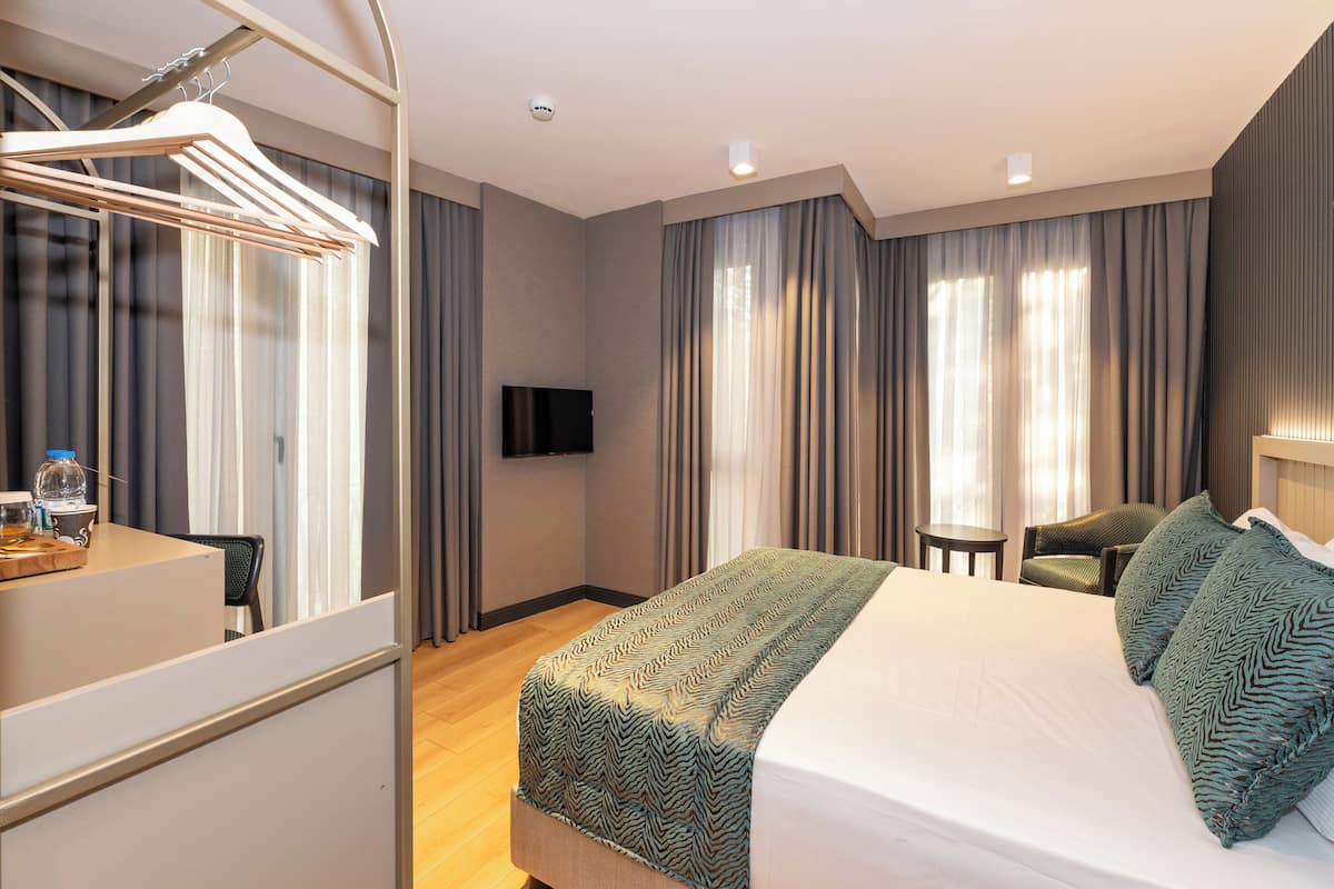 Quarto de hotel com cama, escrivaninha, cadeira, televisão e cortinas.