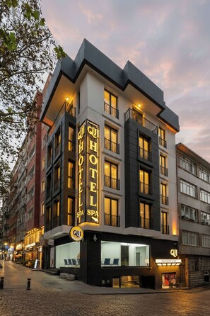 Een hotel met een moderne gevel, meerdere balkons en een opvallend bord dat hotel- en spa-diensten aangeeft.