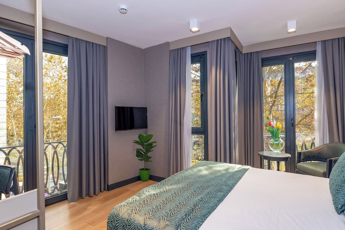 Quarto de hotel moderno com uma cama grande, um vaso de plantas, uma pequena mesa com um vaso de flores e uma cadeira.