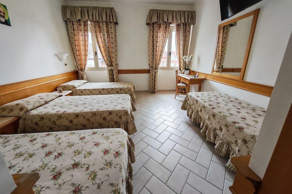 A hotel room with two beds, a desk, a chair, a mirror, and a window with curtains.