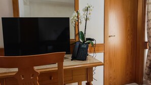 A wooden desk with a flat-screen TV, a telephone, and an orchid. A mirror hangs above the desk, and a door is visible to the right. - Hotel Pace (San Giovanni Rotondo)