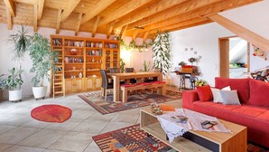 A spacious living area with a wooden ceiling, a red sofa, a wooden dining table, and a bookshelf. - Apartment 'Ferienwohnung am Rosenberg' with Shared Garden, Wi-Fi and Air Conditioning (Stockach)