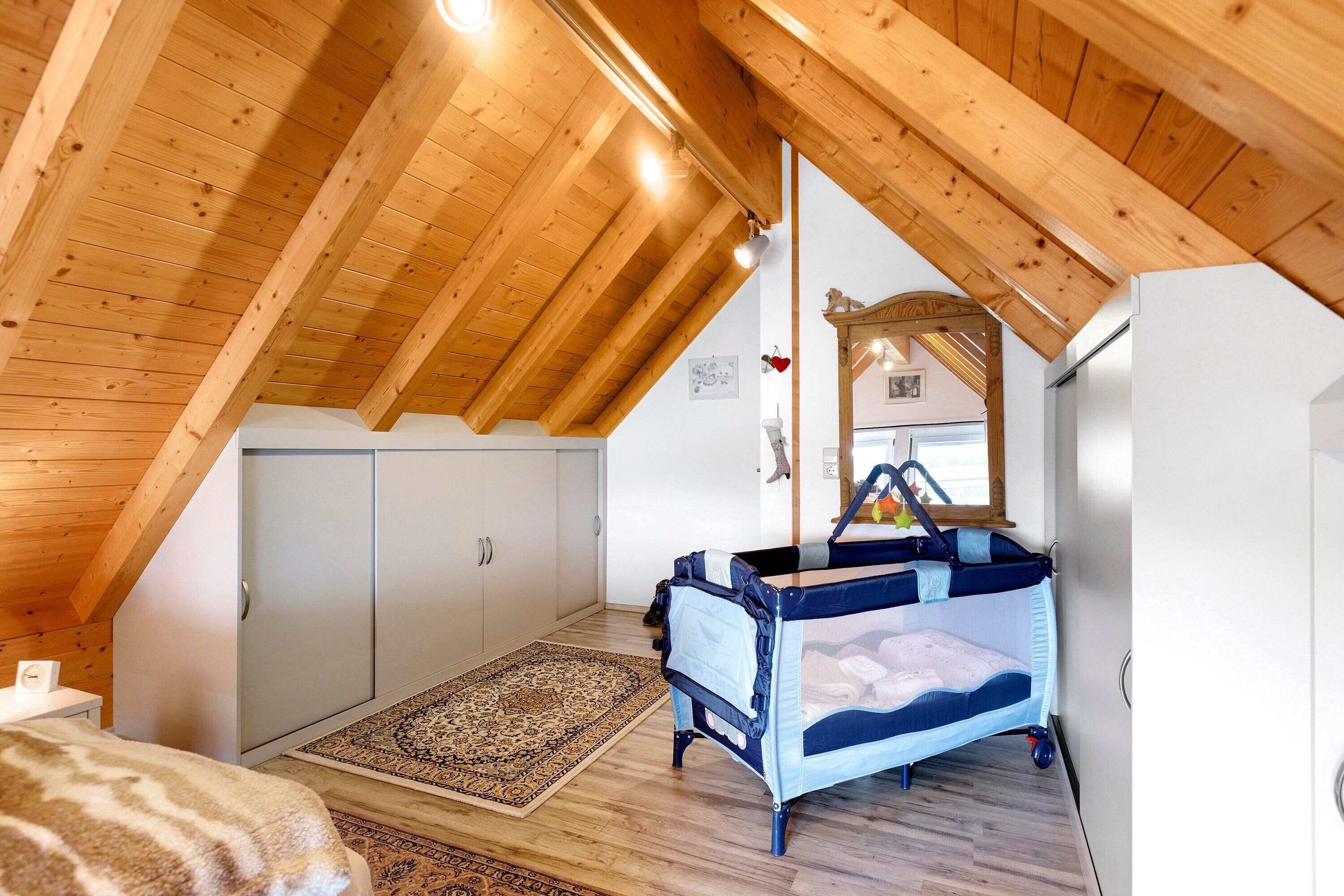 Una habitación con techo de madera inclinado, una cama individual, una alfombra pequeña y un armario.