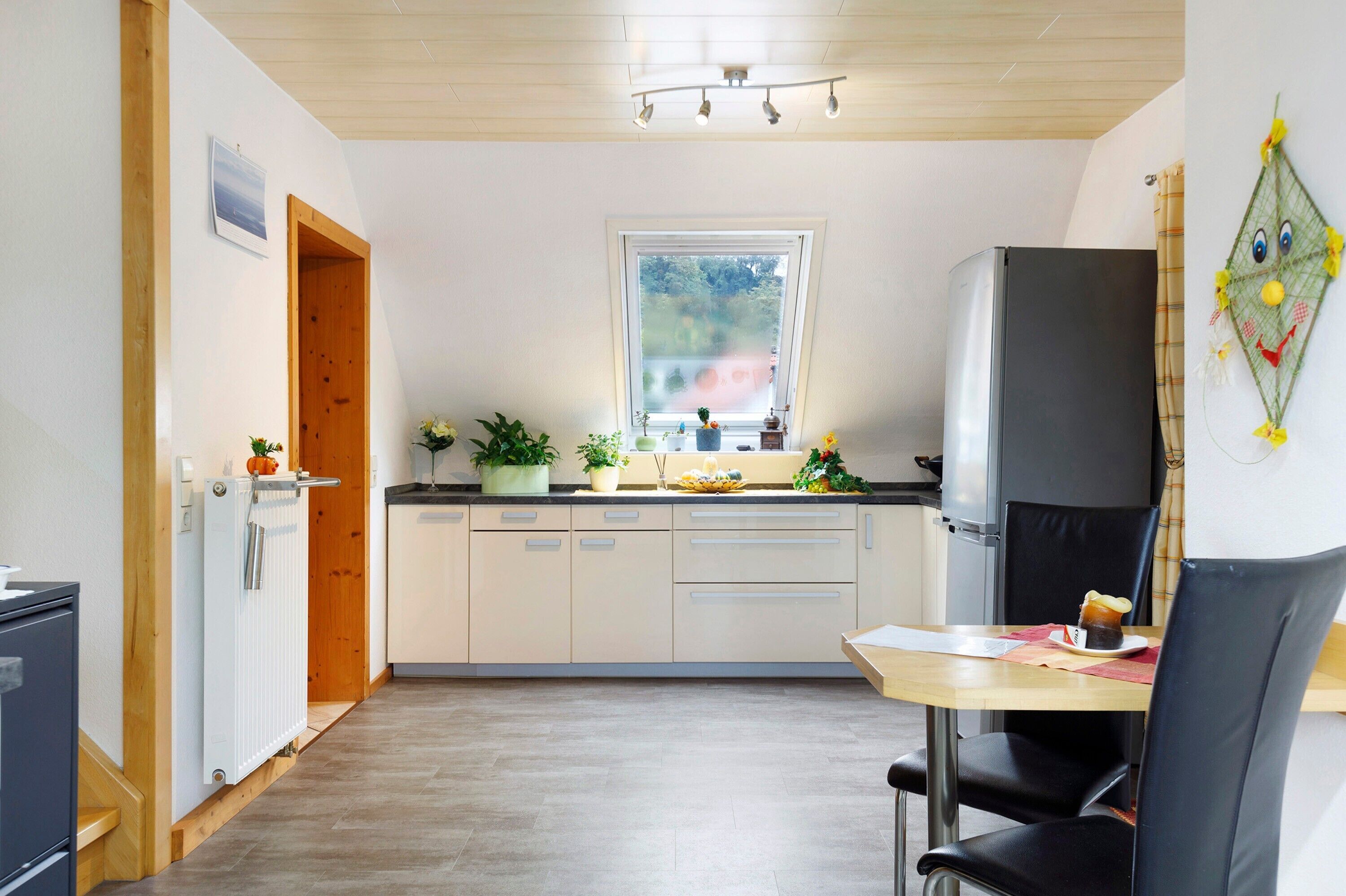 A compact kitchen with a window, a refrigerator, a dining table with chairs, and a radiator.