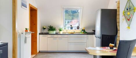 A compact kitchen with a window, a refrigerator, a dining table with chairs, and a radiator.