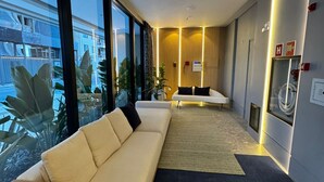 A modern hotel room with a large window, a sofa, a small table, and a bed.