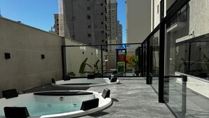 A rooftop pool area with a hot tub and lounge chairs, surrounded by high-rise buildings.