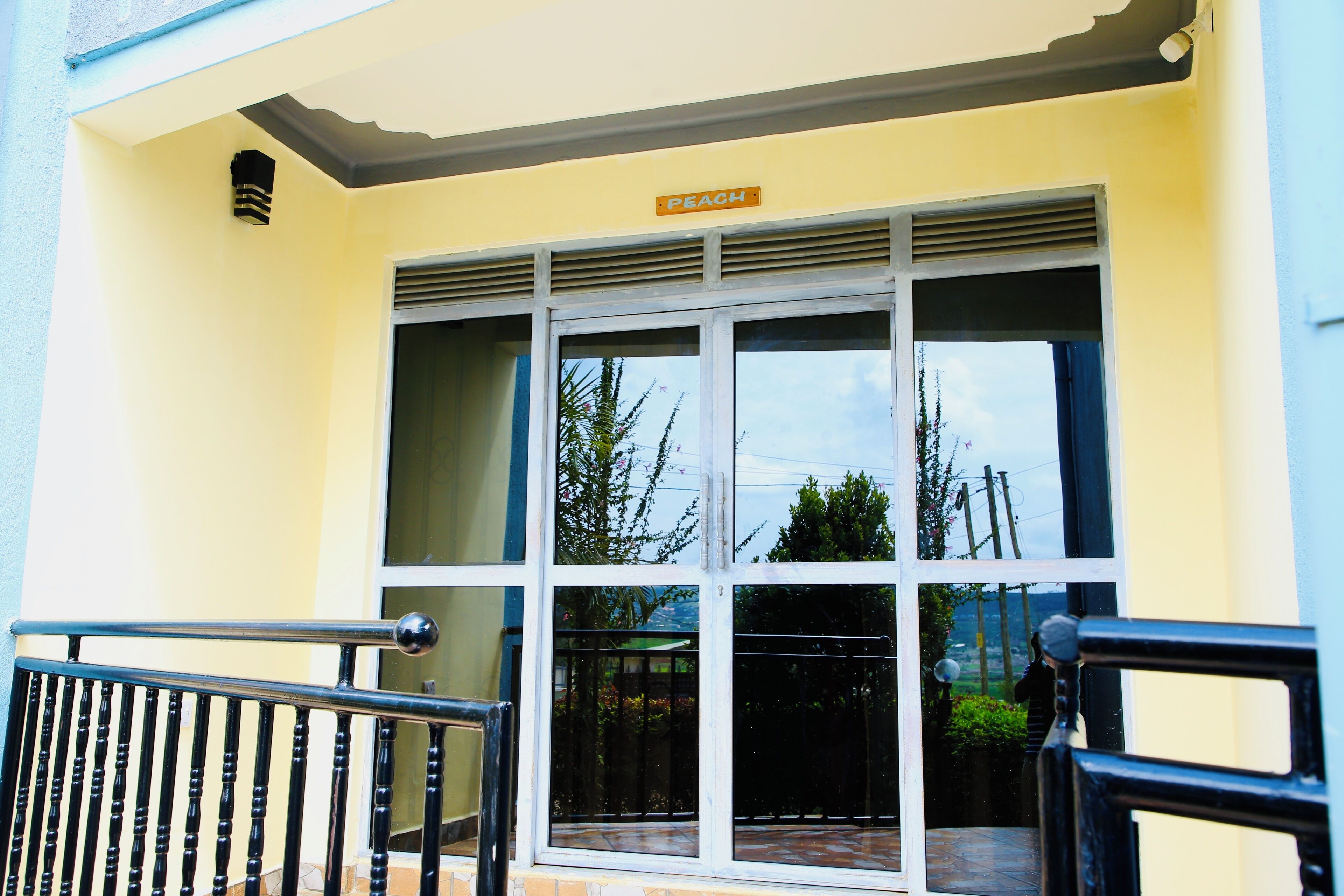A building entrance with a sign reading "PEACH," a large window with a metal grill, and a black metal railing in front.