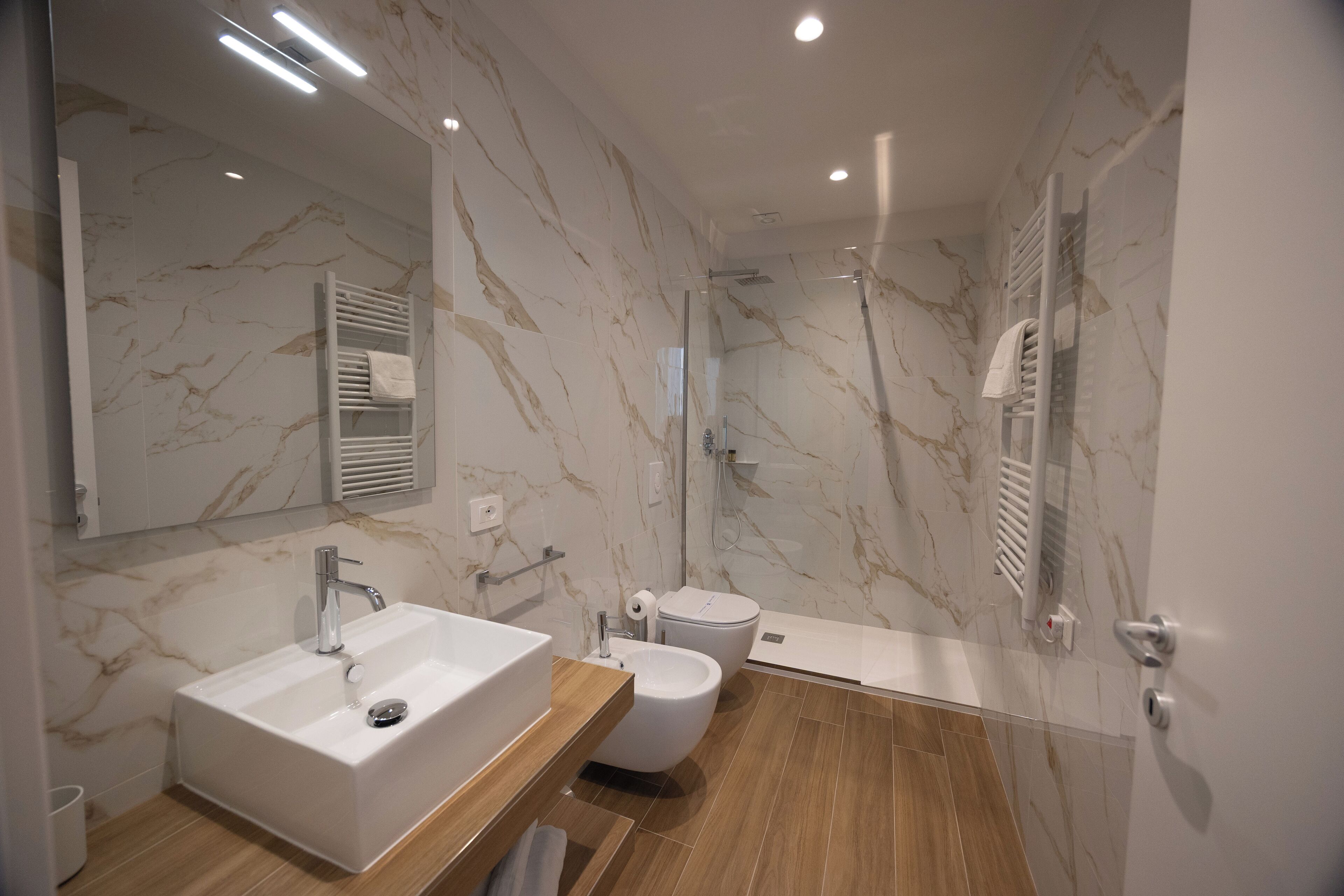 A modern bathroom with a marble backsplash, a freestanding sink, a bidet, and a walk-in shower.