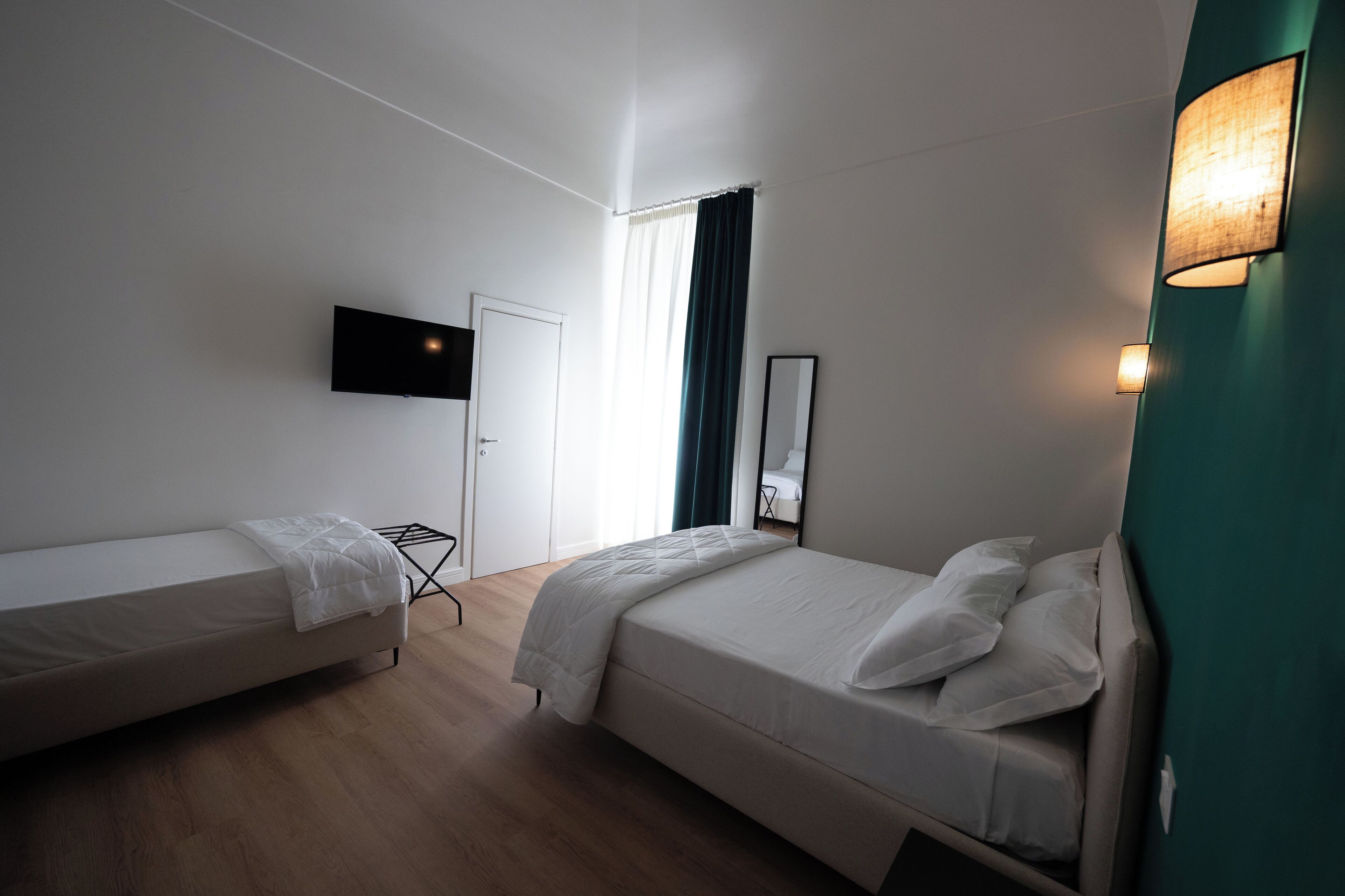 A hotel room with two single beds, a flat-screen TV mounted on the wall, a window with curtains, and a bedside table.