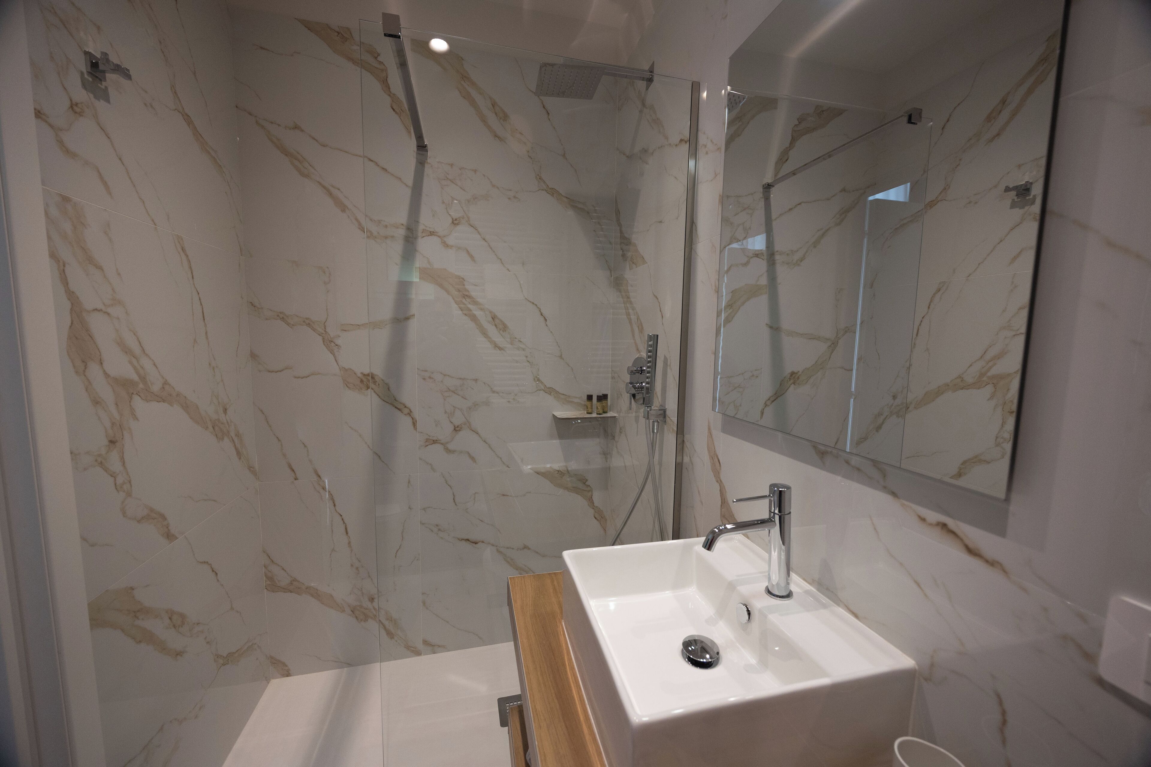 A modern bathroom with a marble wall, a glass-enclosed shower, and a wooden vanity with a sink.