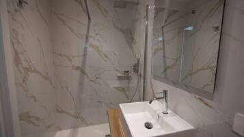 A modern bathroom with a marble wall, a glass-enclosed shower, and a wooden vanity with a sink.
