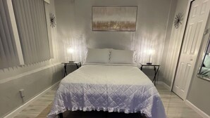 Ein Schlafzimmer mit einem großen Bett, zwei Nachttischen, einem kleinen Tischchen, einem Teppich, einem Deckenventilator und einer Tür.