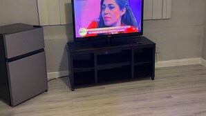 Ein Fernseher auf einem schwarzen Ständer in einem Zimmer mit hellem Holzboden, einem weißen Heizkörper und einer weißen Wand.