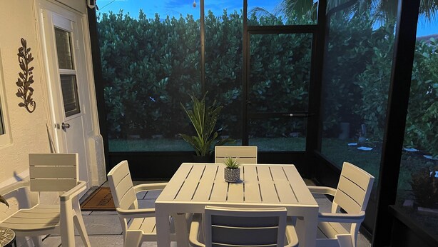 Eine Terrasse mit einem weißen Tisch und Stühlen, einem Blumentopf und Blick auf einen Garten.