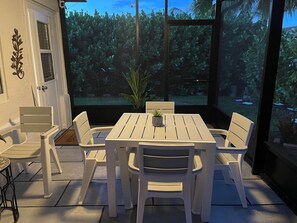 A patio with a white table and chairs, a potted plant, and a view of a garden. - Charming 1-bedroom with private entrance Tamarac. (Tamarac)