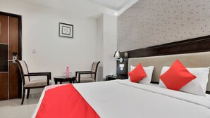 Habitació d'hotel amb un llit, dues cadires, una cambrera de nit, una làmpada i un quadre penjat a la paret.