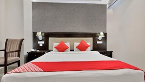 Habitació d'hotel amb un llit gran, dues nits de nit, una cadira i un capçal amb làmpades penjades a la paret.