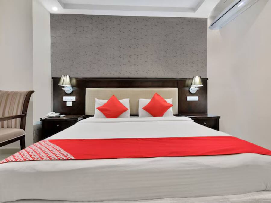 A hotel room with a large bed, two nightstands, a chair, and a headboard with wall-mounted lamps.