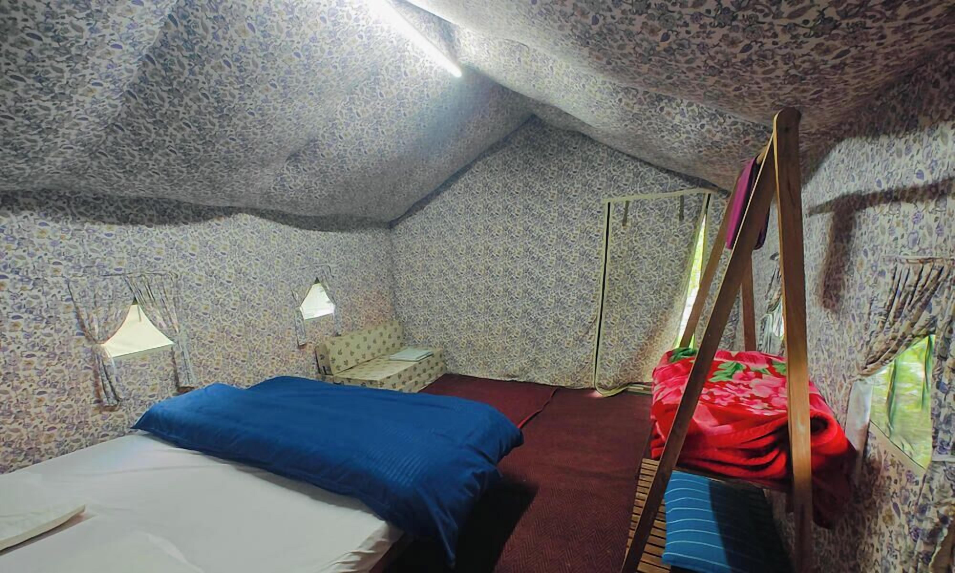 A small, cozy room with a single bed, a nightstand, a lamp, and a window with a view.