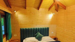 Una habitación de cabaña de madera con una cama, una ventana con cortinas y una lámpara colgante.