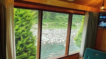 A cabin with a large window overlooking a river, a wooden ceiling, and a green sofa.