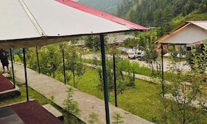 Un espacio al aire libre cubierto con un sendero que conduce a un edificio, rodeado de vegetación y un paisaje montañoso.