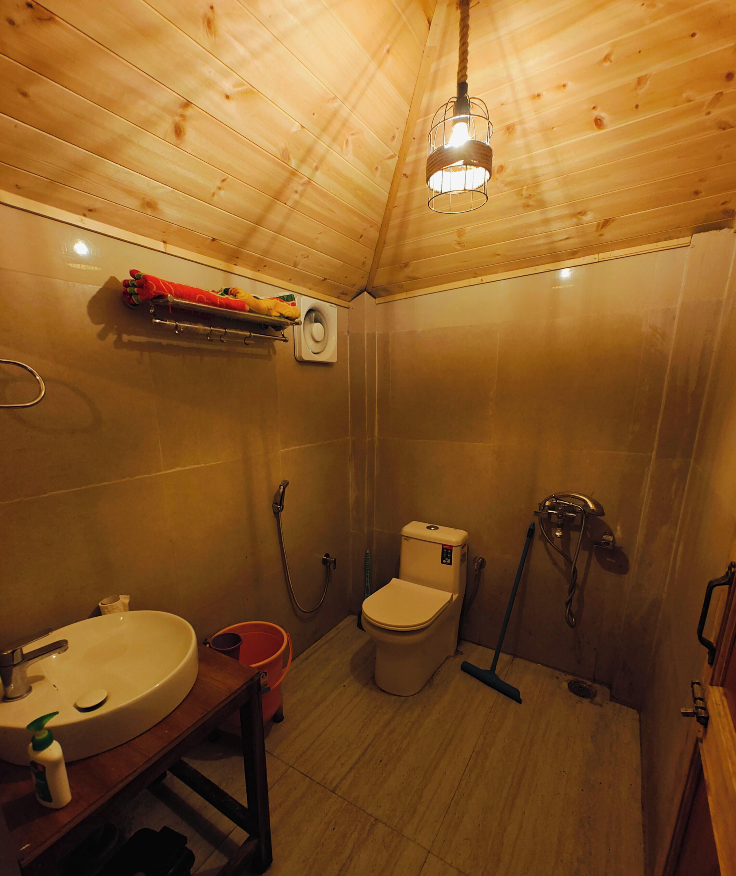 Une petite salle de bain en bois, aménagée dans une cabane, avec un lavabo, des toilettes, une douche et un luminaire suspendu.