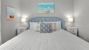 A bedroom with a large bed, two bedside tables, a headboard, and two wall-mounted paintings.