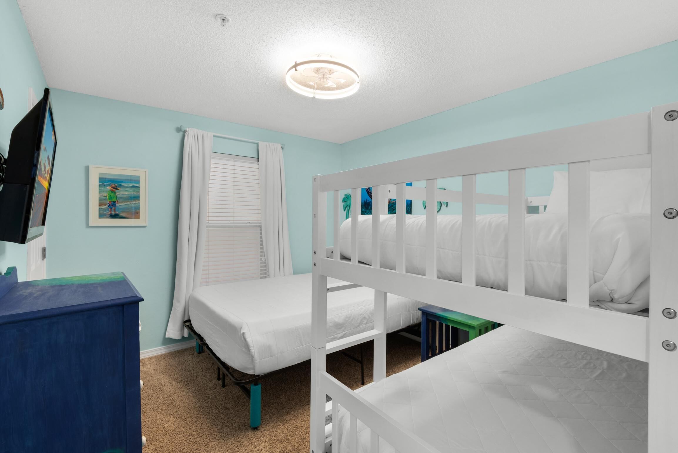 A child’s room with bunk beds, a desk, and a window with curtains.