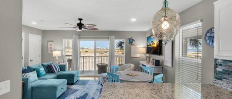 A spacious living area with a teal sectional sofa, a granite kitchen island, and a balcony with a view.