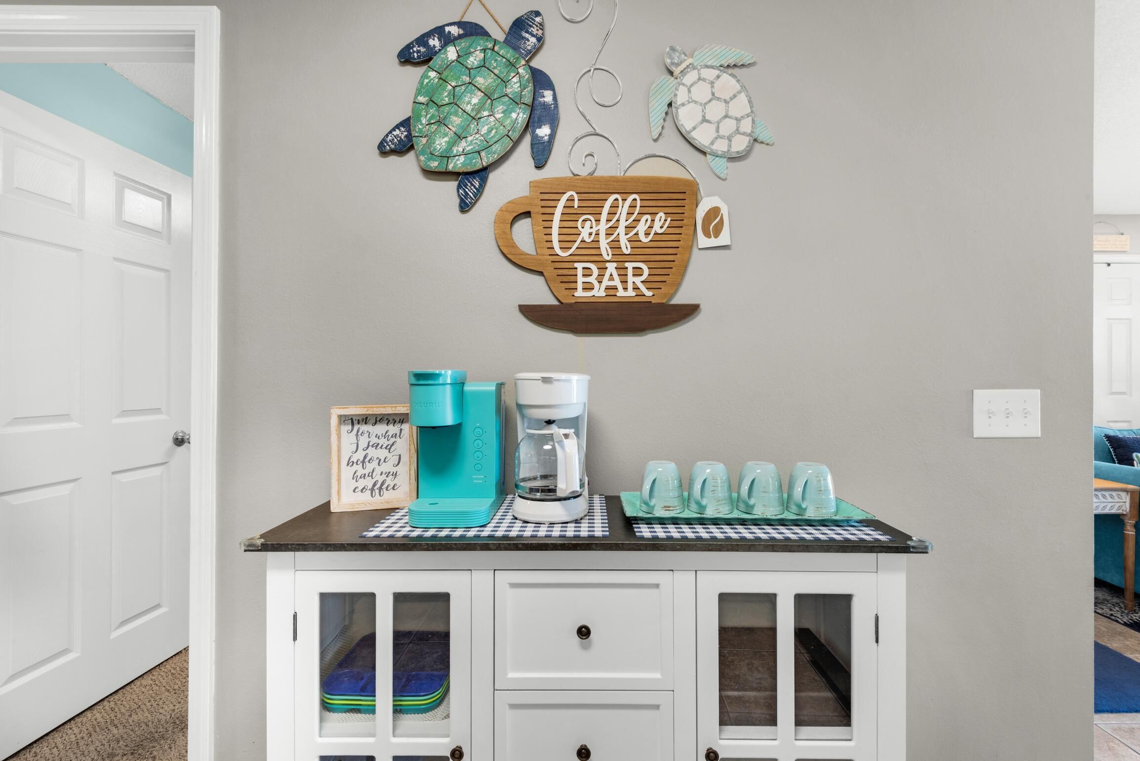 Una zona de cocina con estación de café, que incluye cafetera, tazas y un cartel.