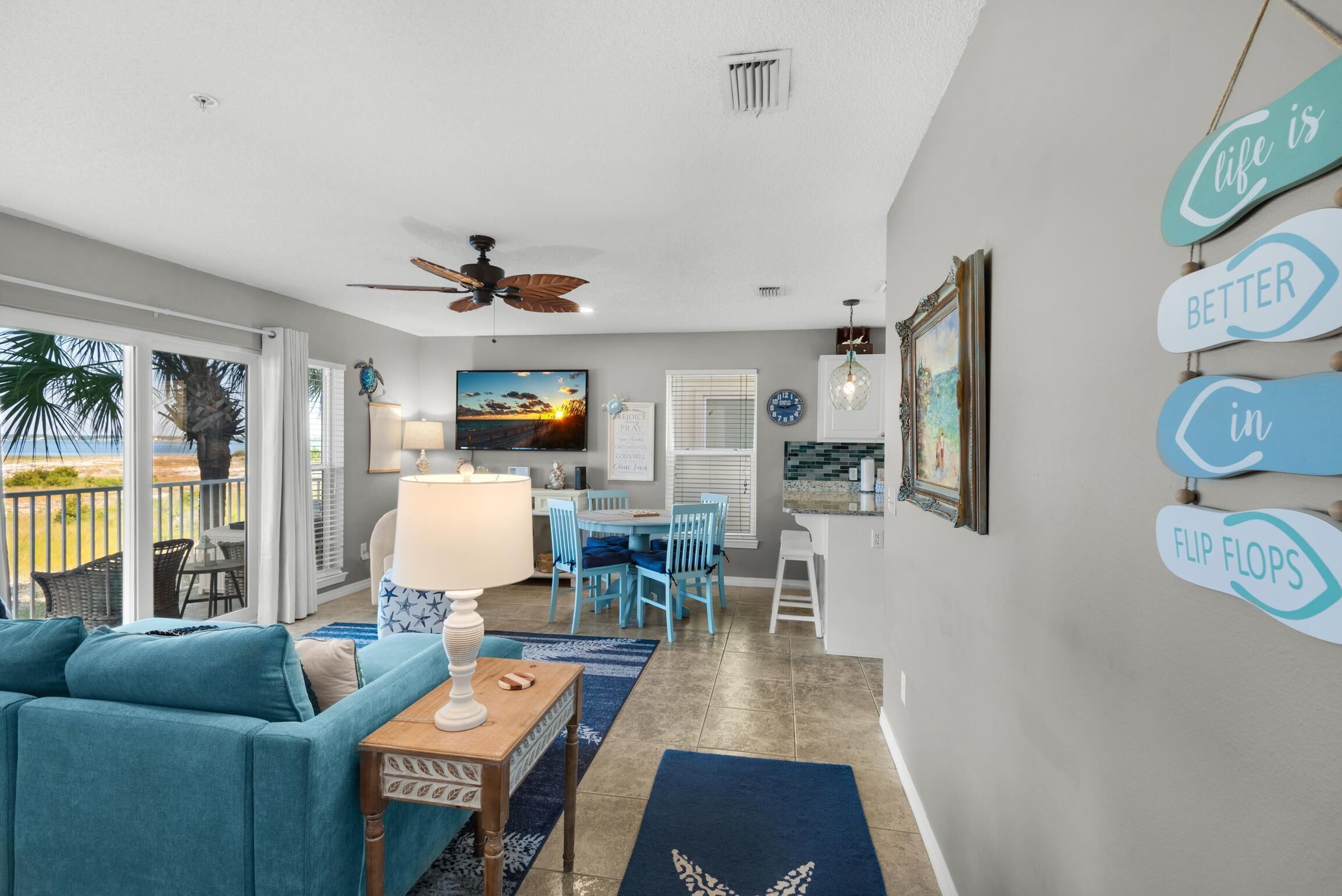 A spacious living room with a teal sofa, a dining area with blue chairs, and a kitchen area with a white countertop.