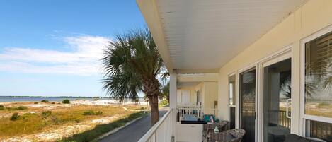 A balcony with wicker furniture, a palm tree, and a view of the beach.