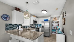 A modern kitchen with a granite island, white cabinets, a stainless steel refrigerator, and a built-in microwave.