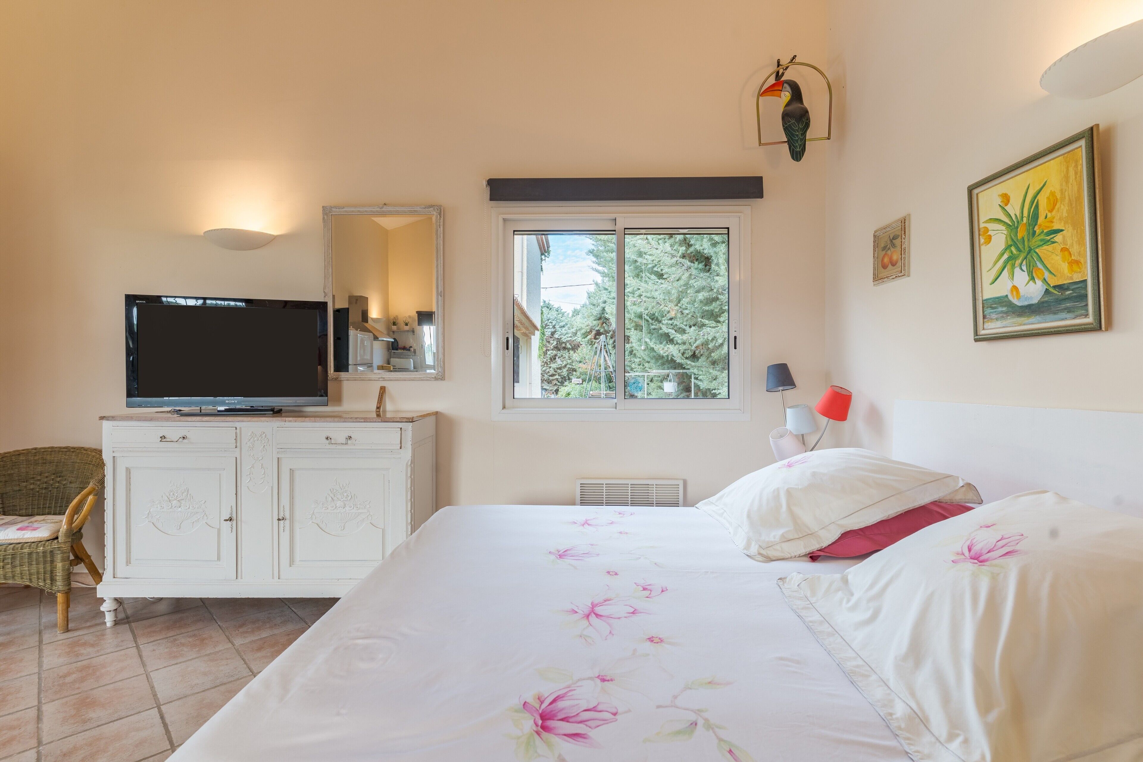 Une chambre à coucher avec un lit, une télévision, une commode, une chaise, une fenêtre et un tableau.