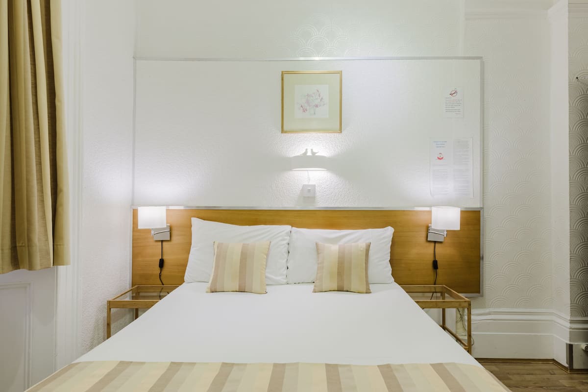 A hotel room with a large bed, two bedside lamps, a wooden headboard, and a framed picture on the wall.