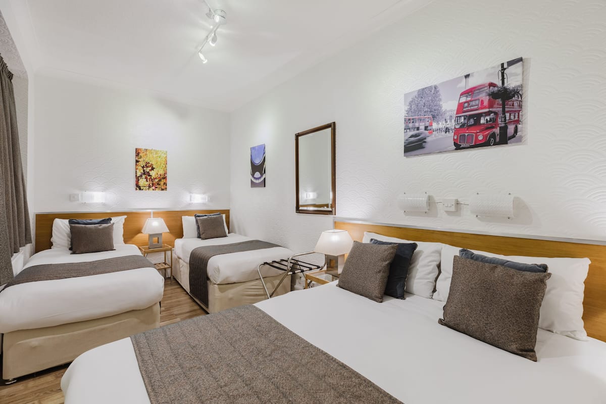 A hotel room with two beds, a large mirror, and a painting of a red double-decker bus.