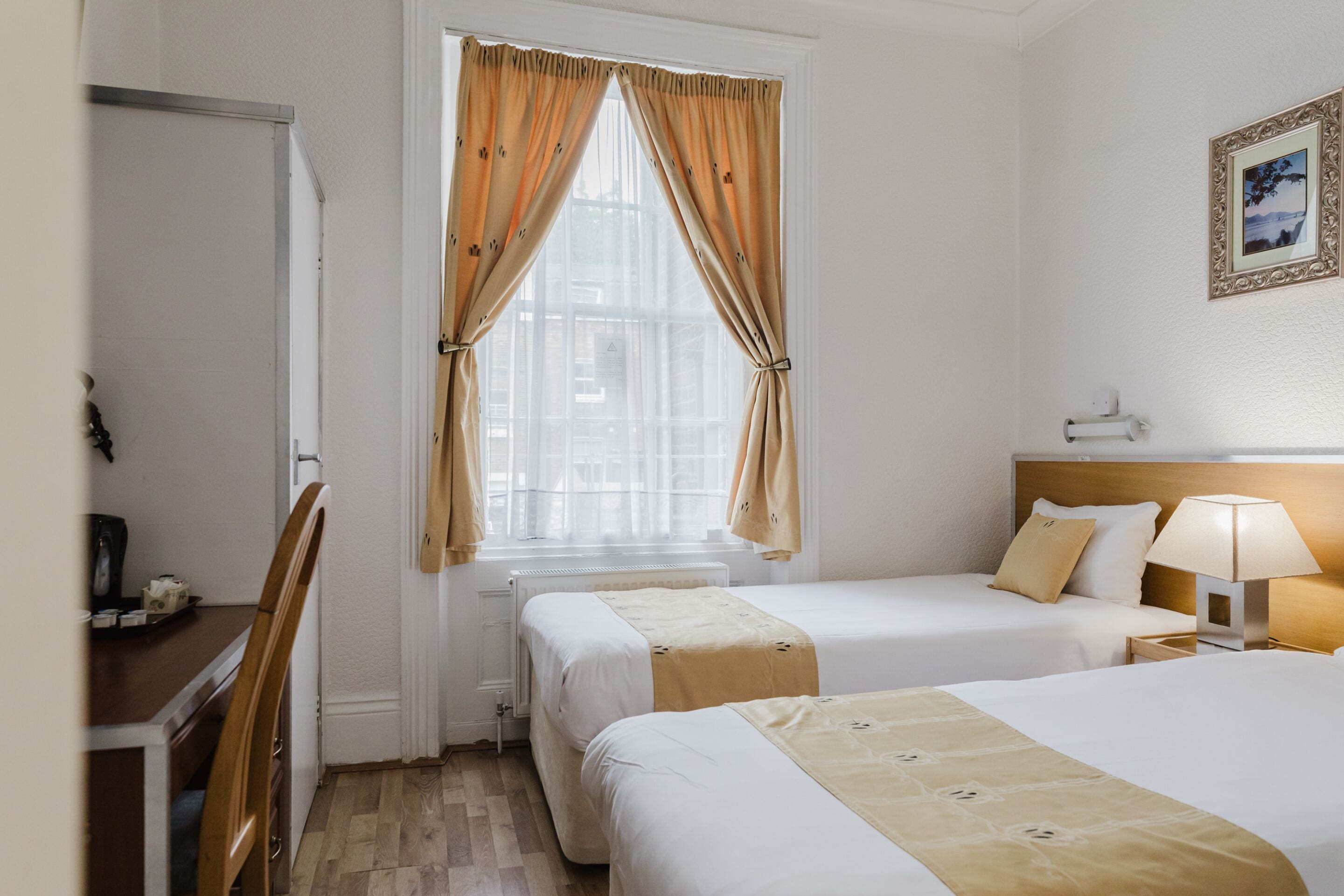Habitación de hotel con dos camas, un escritorio y una ventana con cortinas.