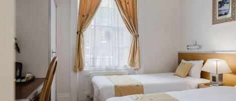 Habitación de hotel con dos camas, un escritorio y una ventana con cortinas.