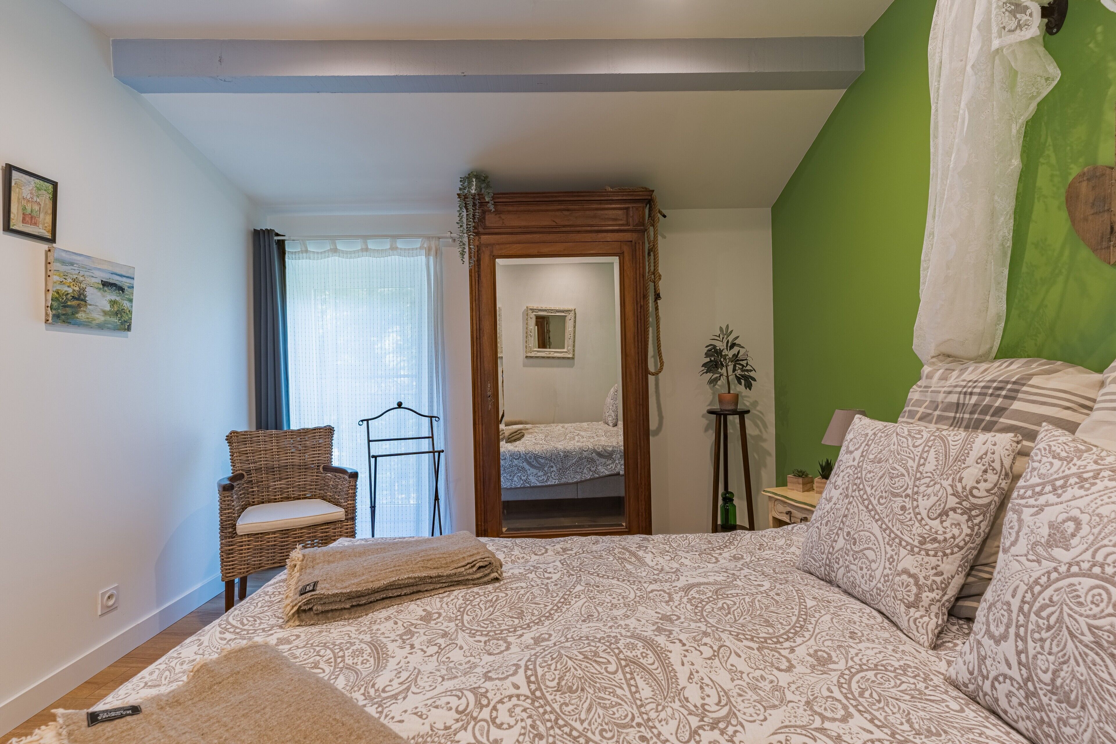 Une chambre avec un grand lit, une chaise, un miroir et un mur vert.