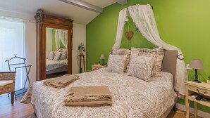 Un dormitorio con una cama grande, un espejo, una pared verde y una mesita de noche pequeña con una lámpara.