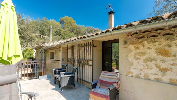 Un patio con mobiliario exterior, una zona de estar cubierta y un edificio de techo de tejas y paredes de piedra.
