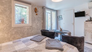 A bedroom with a bed, two chairs, a small table, a TV, and a window with a view of trees.