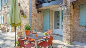 A stone building with a balcony, a table with chairs, and potted plants.