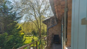 Un balcon doté d’une balustrade en fer forgé, donnant sur un jardin arboré et sur un bâtiment aux murs de pierre.